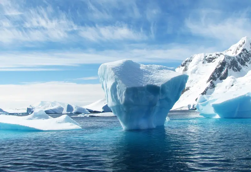 Ledena gora pred zaseneženim pobočjem na obalah Antarktike
